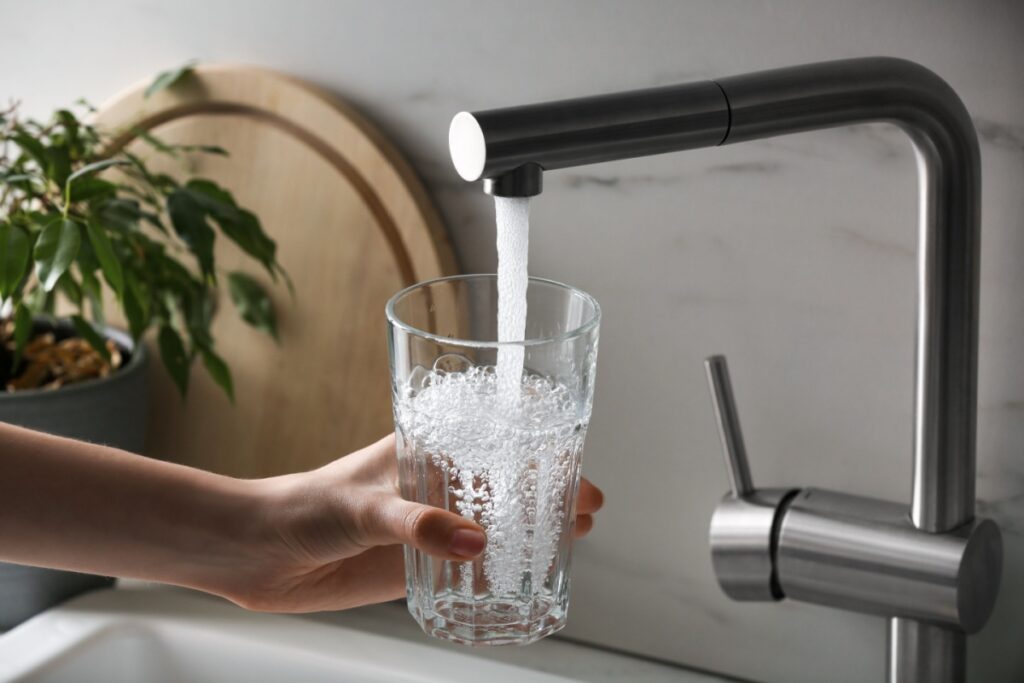 A woman's hand wrapped around a glass as she fills it with tap water from the kitchen faucet