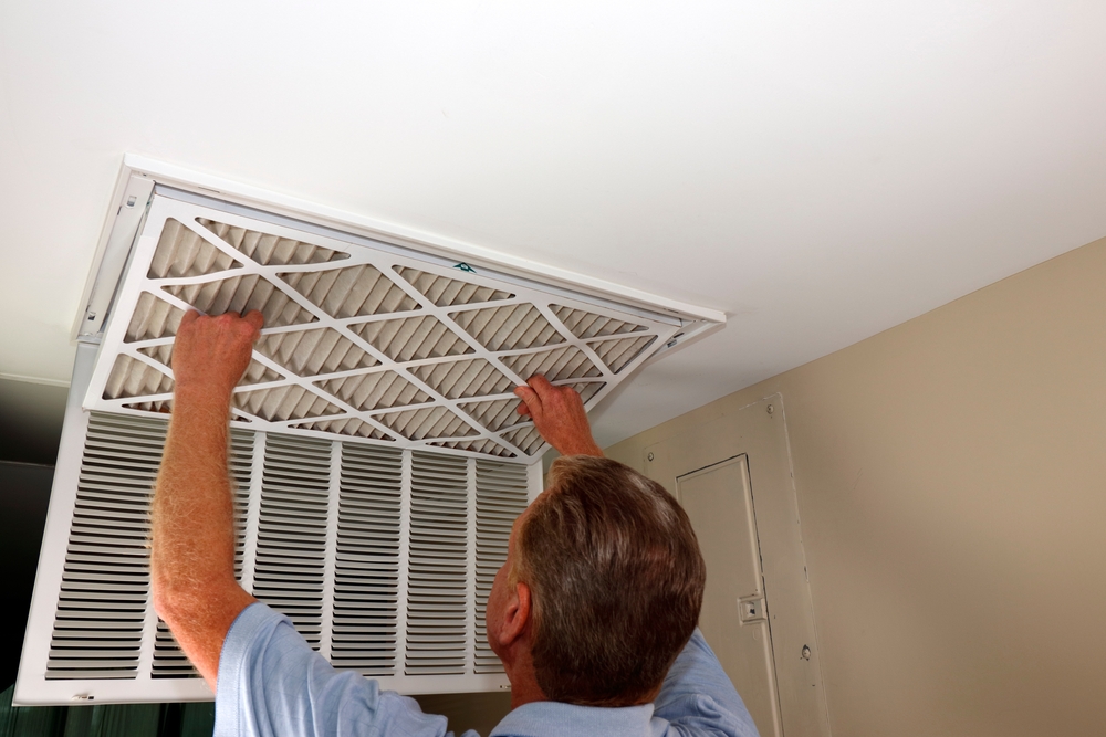 A man removing a dirty air filter from the ceiling to add a high-efficiency filter