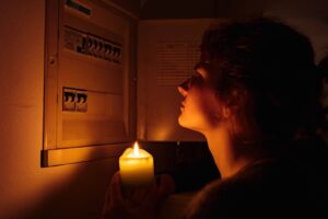 woman looking at an electrical panel in the dark with a candle
