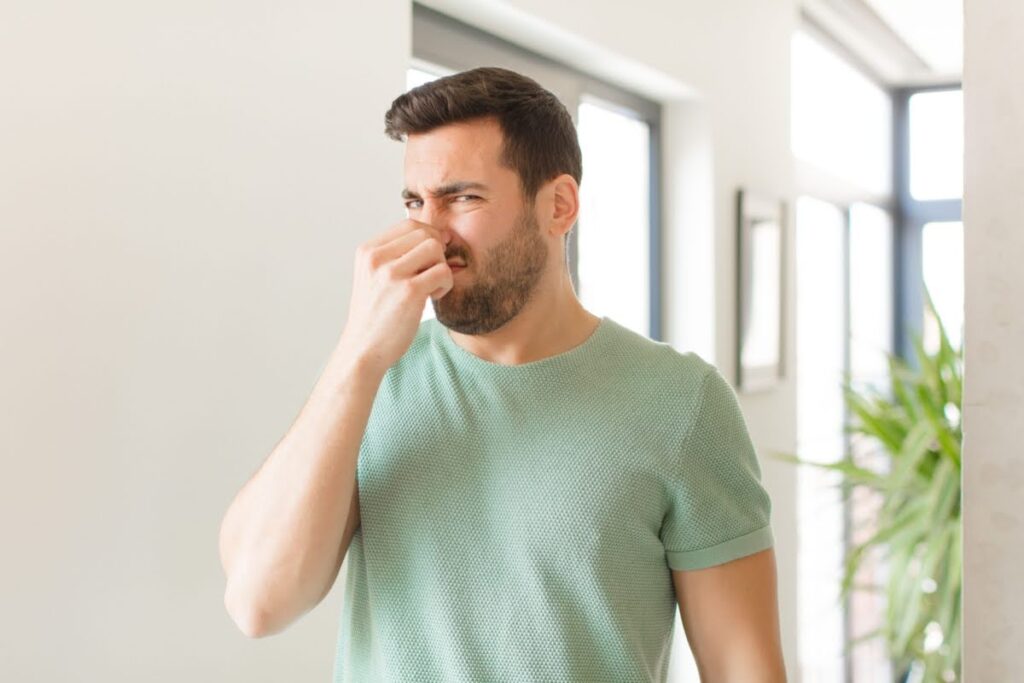 a man holding his nose and scrunching his face because he smells a sewer gas odor in his home