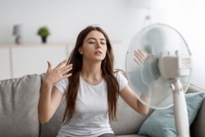 young woman sitting in front of a mini fan because the room is too hot