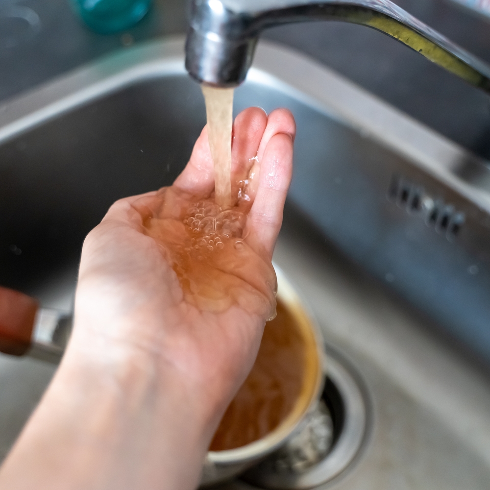 rusty water pouring from the faucet and in pooling in a person's hand