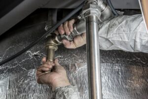 Plumber tightening a metal pipe fitting during plumbing system repair.